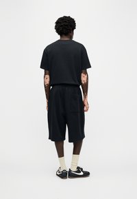 Σετ από μαύρο βαμβακερό μπλουζάκι και σορτς. Το μπλουζάκι έχει στρογγυλή λαιμόκοψη, ενώ το σορτς διαθέτει ελαστική μέση και πλαϊνή τσέπη.