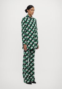 Completo con motivo floreale in verde, nero e bianco. Giacca a maniche lunghe con colletto e pantaloni a gamba larga. Tessuto morbido.