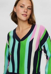 Pleteni pulover z V-izrezom, živahnimi črtami v zeleni, modri, roza in mornarsko modri barvi, sproščenega kroja in mehkega materiala.