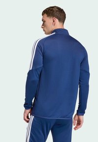 Ναυτική αθλητική ζακέτα με όρθιο γιακά, μακριά μανίκια και λευκές ρίγες στους ώμους. Φτιαγμένη από λείο, κομψό ύφασμα.