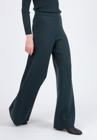 Wide-legged trousers in dark green knit fabric, featuring a smooth texture and high waistband, paired with black footwear.