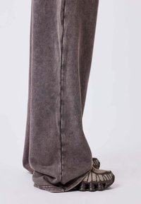Pantalones de tela suave y gris con un corte holgado, que presentan un brillo sutil y puños sueltos, combinados con zapatillas texturizadas y multicolores.