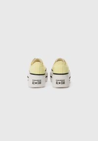 Yellow canvas low-top sneakers with thick white soles, black stripes, and "Converse All Star" branding on the back heel.