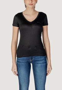 Sort kortærmet V-hals t-shirt lavet af glat stof, med en diskret logo detalje på brystet, parret med lyseblå jeans.