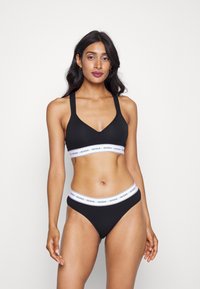 Svart undertøysett som består av en bralette med brede stropper og V-hals, sammen med en matchende bikinitruse. Begge har elastiske strikker med logo.