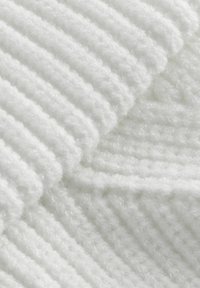 Vit texturerad tyg med ett ribbat mönster, som har mjuka, fluffiga fibrer och varierande djup, vilket skapar ett vågigt utseende.