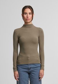 Długi rękaw, top z wysokim kołnierzem wykonany z lekkiej, elastycznej tkaniny w oliwkowym odcieniu. Charakteryzuje się dopasowanym krojem oraz ściągaczami przy nadgarstkach.