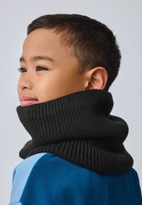 Mustast soonikuga turtleneck kaelus sinise rõiva kohal, millel on struktureeritud, soe tekstuur ja tihe, kihiline disain.