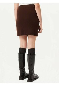 Brun ribbade minikjol med en figursydd design. Bärs med knähöga svarta stövlar och mörka strumpor, vilket framhäver en texturerad look.