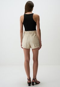 Top in cotone nero a costine abbinato a pantaloni beige con cintura elastica, due tasche posteriori e orlo arrotolato.