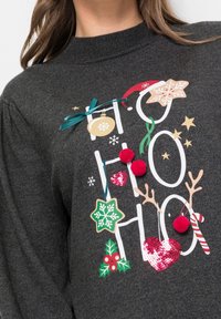 Sudadera gris oscuro con diseño "Ho Ho Ho" que presenta acentos rojos y verdes, pompones, lentejuelas y gráficos navideños.