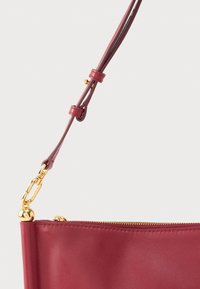 Geantă de mână din piele maro închis cu fermoar auriu, elemente metalice în lanț și curea reglabilă. Textură fină cu detalii minime.