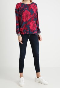 Floral long-sleeve blouse in navy with red flowers, paired with dark skinny jeans and white sneakers. Striped cuffs accent the sleeves.
