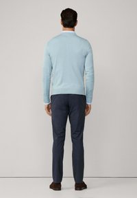 Svetlo modrý dlhý rukáv sveter vyrobený z mäkkej látky, skombinovaný s tmavomodrými nohavicami, z pohľadu zozadu. Hnedé topánky dotvárajú celý outfit.