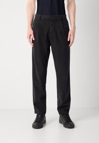 Pantalon noir en mélange de coton avec une coupe décontractée, doté de plis sur le devant et de poches, associé à des baskets noires à lacets.