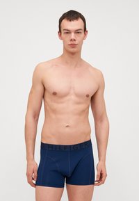 Boxers en coton bleu marine avec une ceinture noire portant le logo 'HILFIGER'. Texture lisse, design ajusté et longueur de jambe courte.