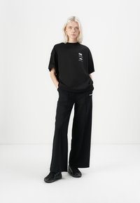 T-shirt in cotone nero a maniche corte con grafica testuale, abbinato a pantaloni larghi neri a vita alta e scarpe sportive nere.