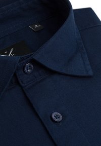 Ciemnogranatowa koszula z teksturowanej tkaniny, z ostrym kołnierzykiem i zapięciem na guziki. Zawiera metkę z informacją o rozmiarze.