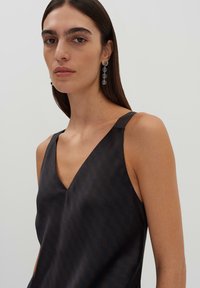 Ärmelloses Oberteil in dunklem Muster mit V-Ausschnitt. Glatter Stoff mit abstrakten Formen. Klare Tropfenohringe vervollständigen den Look.