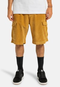 Corduroy cargo shorts i sennepsgul med sidelommer, lige snit og blød tekstur. Bærende med sorte sokker og sneakers.