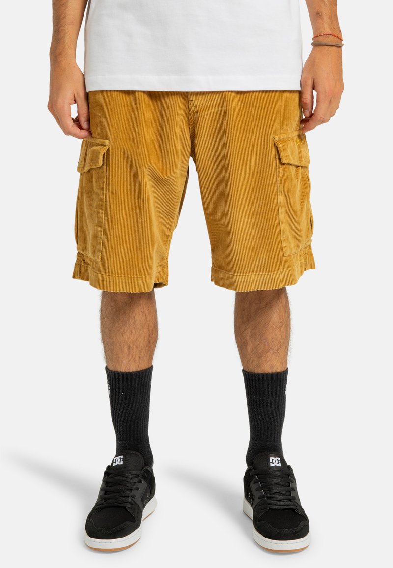 Corduroy cargo shorts i sennepsgul med sidelommer, lige snit og blød tekstur. Bærende med sorte sokker og sneakers.