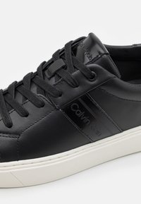 Baskets en cuir noir avec lacets noirs, semelle blanche et logo Calvin Klein sur le côté et la languette.