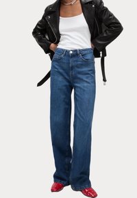 Höga blå denimjeans med avslappnad passform, fem fickor och subtila sömmar. I kombination med en svart läderjacka och röda skor.