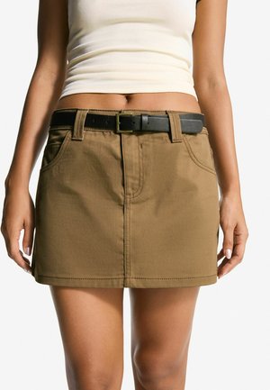 Brown cotton mini skirt with a straight cut, front pockets, and a black belt featuring a rectangular buckle. Smooth texture, casual design.