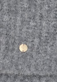 Grijze, gekleurde stof met een gelooide uitstraling heeft een ronde gouden metalen tag met een reliëfletter en twee gaten voor bevestiging.