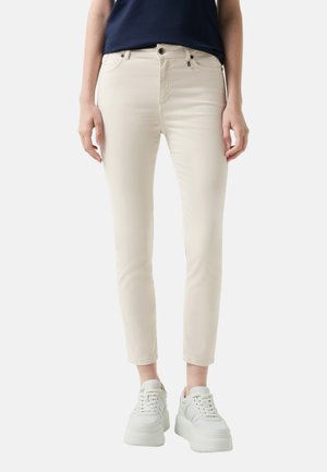 Lysbeige skinny jeans med en mid-rise talje, fem-lomme design og subtile syninger, kombineret med hvide platform sneakers.