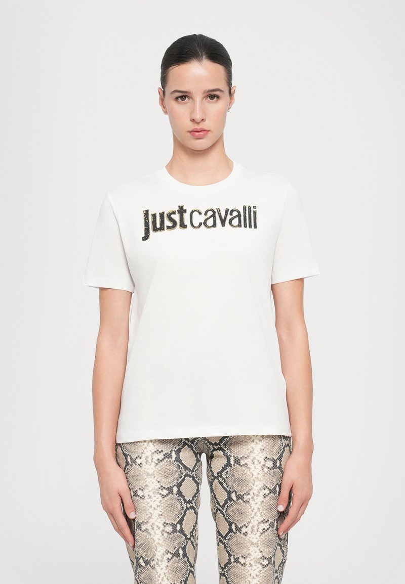 Valge puuvillane T-särk ümarate kaelustega, mille esiküljel on metallikmust "Justcavalli" logo. Koos madu mustriga leggingsidega.