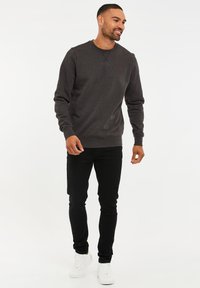 Grauer Pullover mit Rundhalsausschnitt, gerippten Bündchen und Saum. Kombiniert mit schwarzen, enganliegenden Jeans und weißen Turnschuhen, die ein dezentes Logo-Detail aufweisen.