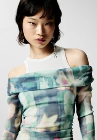 Top s odhalenými ramenami s kvetinovým a abstraktným vzorom v jemných zelených a modrých odtieňoch. Vyrobené z ľahkého materiálu, s textúrovaným dizajnom.