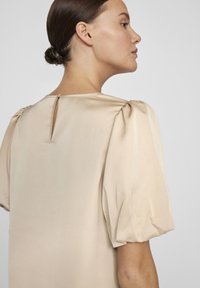Beige puff sleeve tops ar ar smalku satīna apdari, kuram ir atslēgas caurums aizmugurē un smalks šuves plecos.