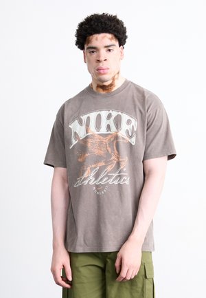 Grey cotton t-shirt with a large, faded white "NIKE" logo and orange winged horse graphic, paired with green cargo pants.