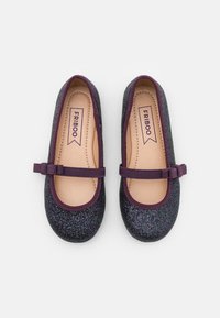 Glitzernde schwarze Ballerinas mit glänzender Oberfläche, lila Besatz und dekorativem Band im Schleifenstil. Das Innere ist glatt beige mit Markenlabel.