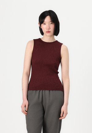 Haut sans manches bordeaux avec une surface texturée, un col rond et une silhouette ajustée, associé à un pantalon gris ample.