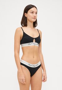 Zwarte bralette met een keyhole ontwerp en dunne bandjes, gecombineerd met bijpassende zwarte bikini slipjes met een witte logo tailleband.
