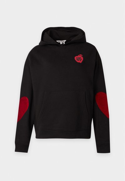 Sweat à capuche noir avec des patchs en forme de cœur rouges sur les coudes et un petit logo pomme rouge sur la poitrine avec le texte "DKNY" à l’intérieur.