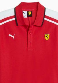 Polo rouge en tissu lisse. Comprend un col noir, des bandes blanches sur les épaules, le logo Puma et l'emblème Ferrari sur la poitrine.
