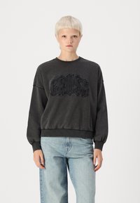 Felpa grigia con la scritta "CRUSH" in rilievo, collo a giro, polsini e orlo a costine, abbinata a jeans azzurri chiari. Design semplice e casual.