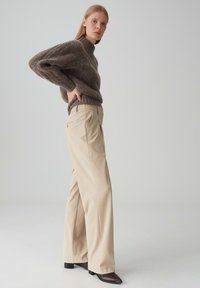 Beige wijde broek met hoge taille, gecombineerd met een gestructureerde grijze trui en dark enkelboots. Gladde stof en een ontspannen ontwerp.