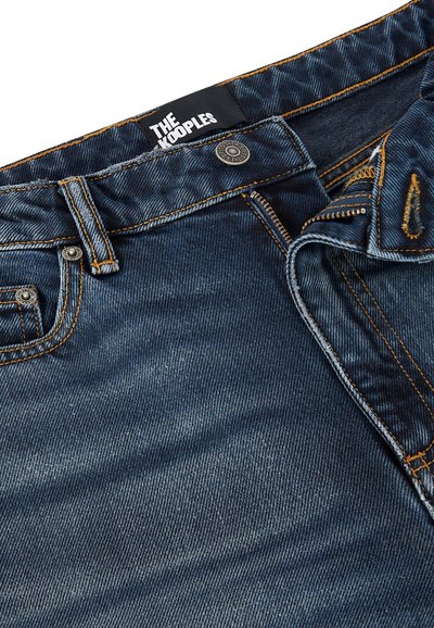 Jeans de mezclilla azul oscuro con costuras naranjas, que presentan un cierre de botón y cremallera, etiqueta en la cintura y bolsillos frontales. Textura suave, zonas desgastadas.