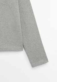 Haut gris à manches longues en tissu doux, présentant une texture côtelée avec un ourlet et des poignets à coupe droite. Aucun motif ou accent visible.