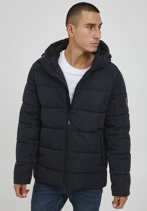 Navy blue padded jacket with a zip front, adjustable hood, and quilted texture. Features two side pockets and logo accent on the sleeve.