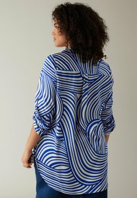 Blusa a righe blu e bianche con un design fluido, maniche arrotolate e orlo curvo. Realizzata in tessuto morbido con un dettaglio tasca frontale.