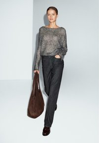 Grå, struktureret sweater parret med mørke denim-bukser. Modellen holder en brun ruskinds tote taske og har mørke sko på. Minimalistisk baggrund.