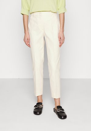 Person iført en lysegrøn top, off-white skræddersyede ankellange bukser og sorte slip-on sko med sølvspænde.