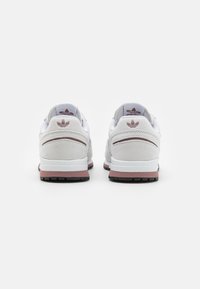 Valkoiset tennarit, joissa on mokkajäljitelmäkoristeet, kangasta, ja vaaleanpunainen välipohja. Mukana on sävyttävä logo kantapäässä ja musta kumipohja.