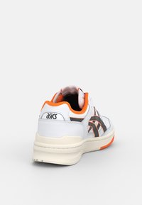 Chaussure de sport blanche avec des accents orange et un logo noir. Caractérisée par une tige en cuir lisse, une semelle en caoutchouc et des détails cousus. Vue arrière présentée.